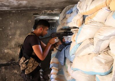 Moawiya Sayasina, the Syrian activist who started scribbling anti-Assad slogans in 2011, aims a Kalashnikov assault rifle through sandbags at a fortified position near the frontline in a rebel-held neighbourhood in the southern Syrian city of Daraa on June 5, 2018. "Your turn, Doctor." Seven years after scribbling the anti-Assad slogan that sparked Syria's war, activists-turned-rebels Moawiya and Samer Sayasina are bracing themselves for a regime assault on their hometown Daraa. / AFP / Mohamad ABAZEED