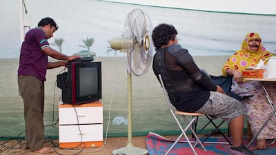 Hamad Al Jasmi and his mother Zahra Al Balooshi relax in the sunshine on the evening before Eid while Qassim Mohammad, one of the family's employees, sets up a television.