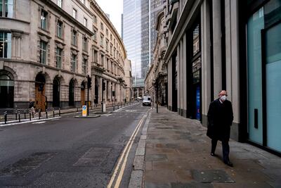 A man wears a face mask while walking in an empty street in the London's financial district, known as The City, as new work from home guidance came into effect. AP.