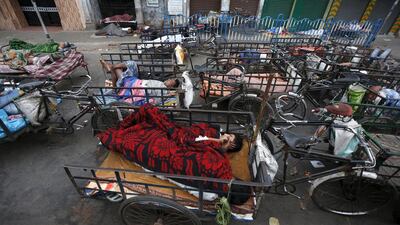 Cycle rickshaw drivers sleep in their rickshaws along a roadside early morning.