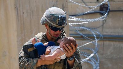 A US marine cradles an infant while waiting for the mother to return during an evacuation at Hamid Karzai International Airport. Reuters