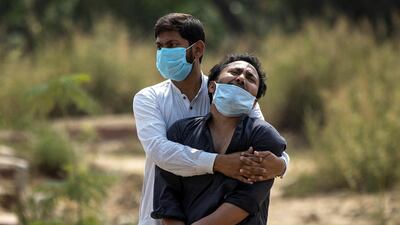 A man is consoled by a relative as he sees the body of his father, who died from Covid-19, in a graveyard in New Delhi, India. Reuters