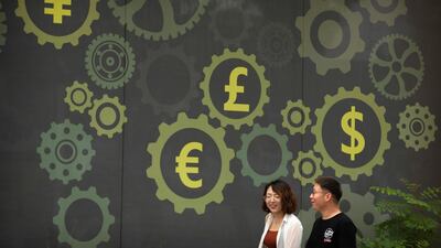 People walk past a mural showing symbols of world currencies in Beijing. The US-China trade war has crimped the global economy's growth, according to the World Bank and IMF, and its reverberations are affecting energy markets and economies of the Middle East and North Africa. AP