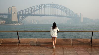 A woman looks at the Sydney Harbour Bridge and central business district shrouded in haze. Bloomberg
