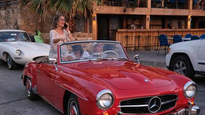 A woman sits in a two-door 1961 Mercedes Benz 190 SL during a parade at the port.