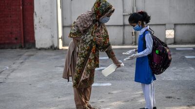 A teacher sprays disinfectant on the shoes of a child at the entrance of a junior campus school upon arrival in Islamabad. AFP