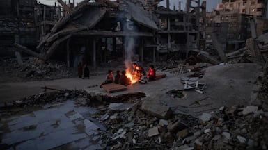 Gazans warm themselves by a fire in the ruins of their home in Khan Younis. EPA