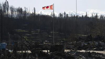 A picture taken on May 14, 2016 showing the Canadian flag flying over damage caused by a wildfire that swept through several neighbourhoods in Fort McMurray, Alberta, Canada. Alberta health services has issued an air-quality advisory for the Fort McMurray area. Handout from government of Alberta/EPA