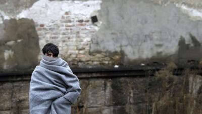 A refugee wrapped in a blanket walks in front of an abandoned warehouse in Belgrade, Serbia, on December 20, 2016. Darko Vojinovic/AP Photo