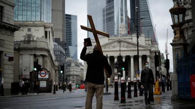 A man holding a cross and a Bible preaches about Christianity backdropped by the Royal Exchange, back centre, and the Bank of England, at left, during England's second coronavirus lockdown in the City of London. AP Photo