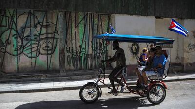 A rickshaw passes by a graffiti of street art in Havana.
