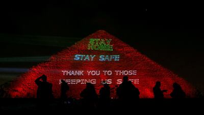 People are seen in front of the pyramid of Khufu, the largest of the Giza pyramid complex, illuminated with text encouraging people to stay home, as Egypt ramps up its efforts to slow down the spread of the coronavirus outbreak, in Giza, on the outskirts of Cairo, Egypt. Reuters