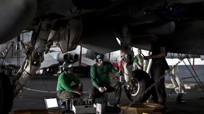 Aircraft mechanics, wearing green jerseys, perform maintenance on the landing gear of a fighter jet inside the hangar on board the carrier.