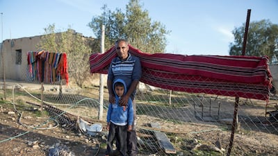 Ali Galboa stands with his son against a traditional carpet hung from the fence that surround his home in Al Poraa on February 4, 2018. Heidi Levine