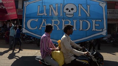 Indian motorists drive past a poster bearing the name of Union Carbide, the company responsible for the gas leak in 1984 which killed at least 15,000 people over the years. Indranil Mukherjee / AFP Photo