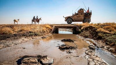 Youths ride donkeys near a US military vehicle crossing a stream polluted by an oil spill near the village of Sukayriyah, in the countryside south of Rumaylan in Syria's Kurdish-controlled northeastern Hasakeh province. AFP
