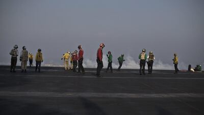 Flight deck personnel, wearing different coloured shirts to distinguish their tasks, are seen on the deck.