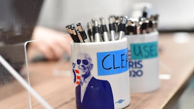 A lab technician works behind pens placed in themed President-elect Joe Biden mugs that state "CLEAN" and "USED" at a coronavirus (COVID-19) testing location for media in Wilmington, Delaware. AFP