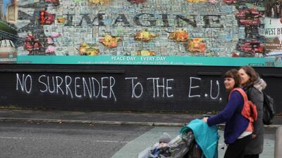 In this photo dated Monday Oct. 14, 2019 people walk past pro-Brexit graffiti in West Belfast Northern Ireland. Fears about a return to the violence that killed more than 3,500 people over three decades have made Northern Ireland the biggest hurdle for U.K. and EU officials who are trying to hammer out a Brexit divorce deal. (AP Photo/Peter Morrison)