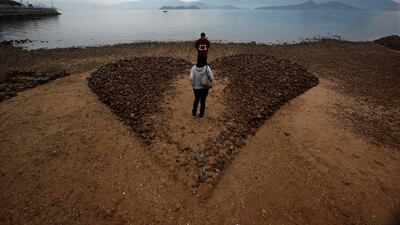 A man shows a tablet computer, with its screen displaying "I love you" in Chinese, to his girlfriend on a heart-shaped sculpture made of six by seven metres of sand and stone, during low tide at a beach in Hong Kong on Valentine's Day February 14, 2012. ???
