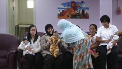 A mother hands her baby to one of the Al Mafraq Juvenile Welfare Centre staff, as they pose for a picture with the babies in the main hall. Five nannies from the Philippines care for children at the centre. Silvia Razgova / The National