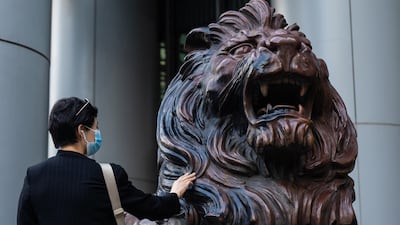 A person wearing a protective mask touches a statue of a lion in front of the HSBC's headquarters in Hong Kong on Thursday. Damaged and defaced during tumultuous protests at the start of this year, the two bronze lion statues standing guard outside HSBC's main office in Hong Kong, made their return to the public. Bloomberg