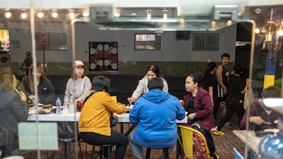 Customers sit side by side with strangers at two long tables on the pavement