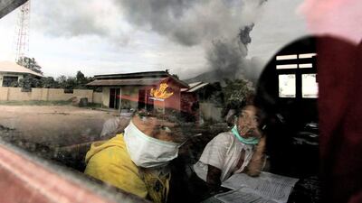 Schoolchildren wear masks while studying in a classroom in Karo district, North Sumatra province Mount Sinabung is seen spewing out volcanic ash through the school window. Fatima Elkareem / AFP Photo