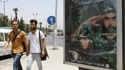 Two men walk past a billboard in the Syrian capital Damascus, which calls on young men and women to enlist in the country's army. Louai Beshara/AFP Photo