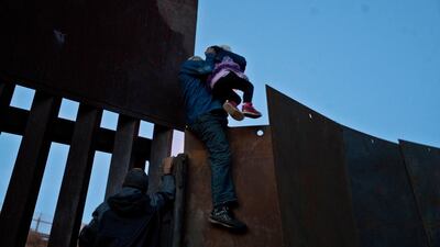 A Honduran migrant helps a young girl cross to the American side of the border wall, in Tijuana, Mexico. AP Photo