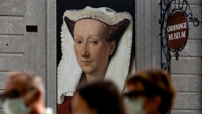 A group of people, wearing protective face masks, walk by an exhibition advertisement for the Groeninge Museum in Bruges, Belgium. AP Photo