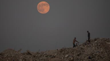 Palestinian children collect plastic from the garbage as a full moon rises over Khan Younis camp in the southern Gaza Strip. EPA