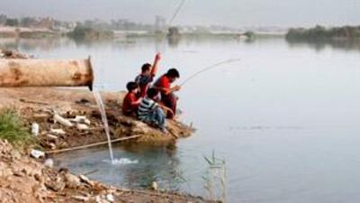 Young men fish next to a sewage pipe in the polluted Tigris River in central Baghdad.