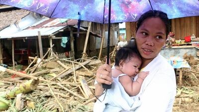 A woman stands with her infant child in front of homes damaged in eastern Samar, Philippines. Rescuers used bulldozers to dig through mountains of mud in the search for more than 40 people missing in the eastern Philippines after landslides triggered by a powerful storm which killed at least 31 at the weekend. Alren Bernonio / AFP Photo