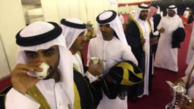 Bridegrooms, wearing the traditional gold-embroidered bisht, take coffee before their mass wedding at Liwa during the date festival.
