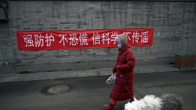 A woman with a face mask walks a dog past a banner on a wall in Beijing, China. Reuters