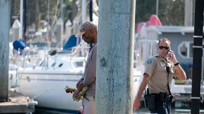 James Miranda, left, of Santa Barbara, holds flowers and takes a moment to reflect at a dock near the Sea Landing at Santa Barbara Harbor. AP