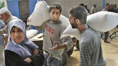 A Palestinian woman waits as others collect food aid at a United Nations distribution center in the Shati refugee camp in Gaza City, Thursday, Nov 20 2008. Israel's tightening Gaza blockade, a response to Palestinian militant rocket fire, has led to frequent blackouts throughout Gaza and resulted in shortages of food, supplies and even cash.