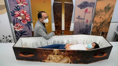 Wilson Tong, CEO of LifeArt Asia, left, talks to a reporter who tries out a catholic-designed paper coffin at Tong's factory in Hong Kong, Friday, March 18, 2022. Hong Kong is running short of coffins during its deadliest outbreak of the coronavirus pandemic, which has cost about 6,000 lives so far this year. LifeArt, a company in Hong Kong is trying to make an alternative, cardboard coffin, which it says is environmentally-friendly. (AP Photo / Kin Cheung)