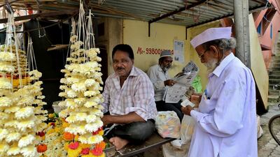 A Muslim man, centre, reads a newspaper as a Hindu man buys flowers from a vendor at a market in Belagavi, India, on October 7, 2021. AP