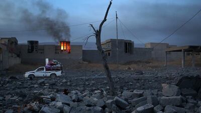 People remove household goods from the rubble of their town as a house burns in Sinjar, Iraq.