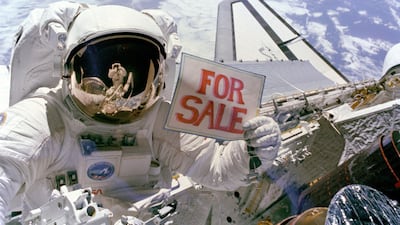 Astronaut Dale A. Gardner holds up a "For Sale" sign referring to the two satellites, Palapa B-2 and Westar 6 that were retrieved from orbit by the Discovery crew. A portion of each of two recovered satellites is in the lower right corner, with Westar 6 ???