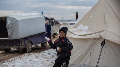 A child makes snowballs and throws them inside the camp.