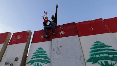 An anti-government protester and his daughter stand on a concrete wall installed by authorities to keep protesters far from the main Lebanese government headquarters and open the road to parliament, in downtown Beirut, Lebanon. AP Photo