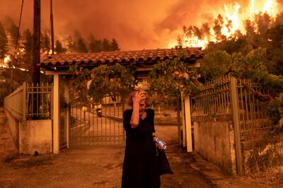 A woman flees her house in the Greek village of Gouves as a wildfire approaches.