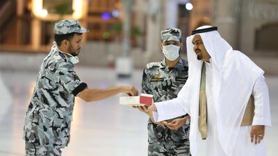A worshipper offers sweets to a security guards, some with face masks, during Eid Al Fitr prayers at the Grand Mosque. AFP
