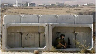 An Israeli soldier sits behind concrete blocks in the village of Ghajar on the Israeli-Lebanese border, where Israel is withdrawing troops.