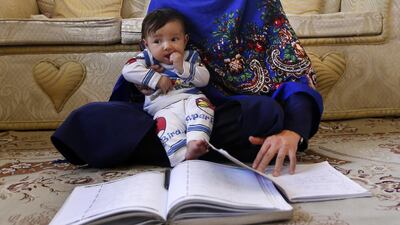 An Afghan mother holds her youngest child while reading a book at their house in Kabul, Afghanistan. Hedayatullah Amid / EPA