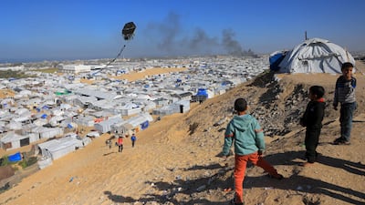 Boys flying a kite watch as smoke rises from the shelter that housed displaced Palestinians after an Israeli bombing of Khan Younis