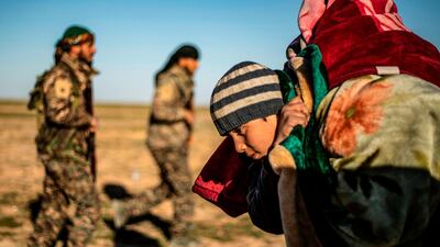 A child walks carrying covers on his back past members of the Kurdish-led Syrian Democratic Forces (SDF) after leaving ISIS's last holdout of Baghouz, in the eastern Syrian Deir Ezzor province on March 1, 2019. AFP